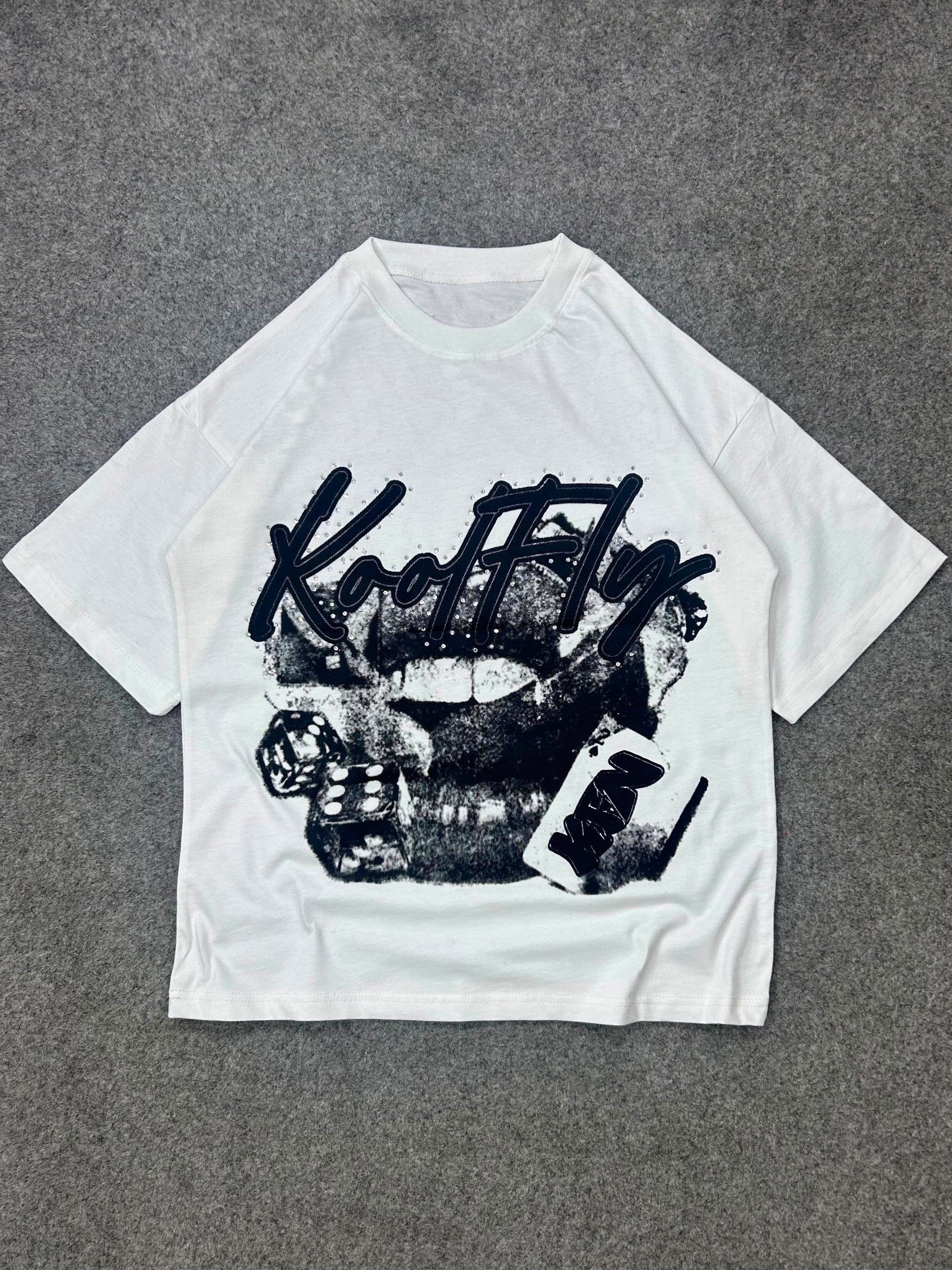 A white short-sleeve t-shirt with a black graphic print featuring the text 'Kool Fly' and a women's mouth design, laid flat on a gray textured background.